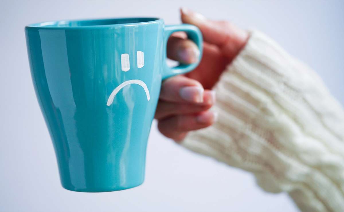 Tazza azzurra con un'espressione triste disegnata, tenuta da una mano con maglione bianco, simbolo del Blue Monday